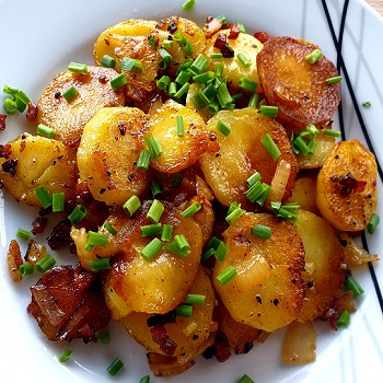 German fried potatoes on top of a white plate with green onion as garnish.